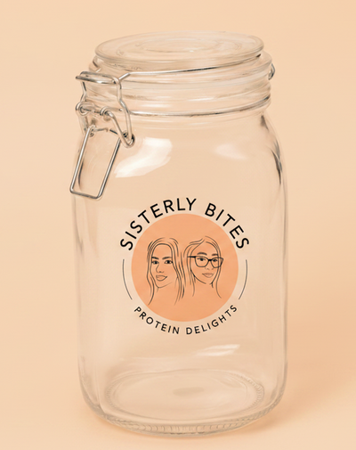 A clear glass clamp-lid jar with a metal wire bail and screw-top lid, featuring a circular peach-colored label that reads 'SISTERLY BITES PROTEIN DELIGHTS' with illustrated faces. The jar is photographed against a solid warm beige background.